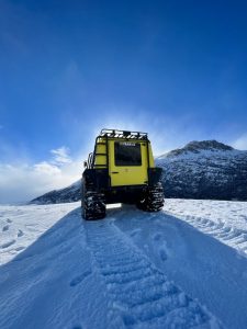 Fat Truck 2.8 Wagon in custom yellow Team CC livery on an arctic alpine snowfield with dramatic mountain ridges showing 4x4 amphibious vehicle extreme cold weather capability